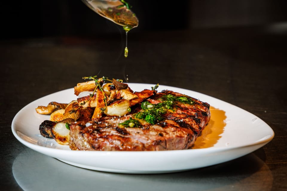 A chef plating a seared steak on the line at The Alexander