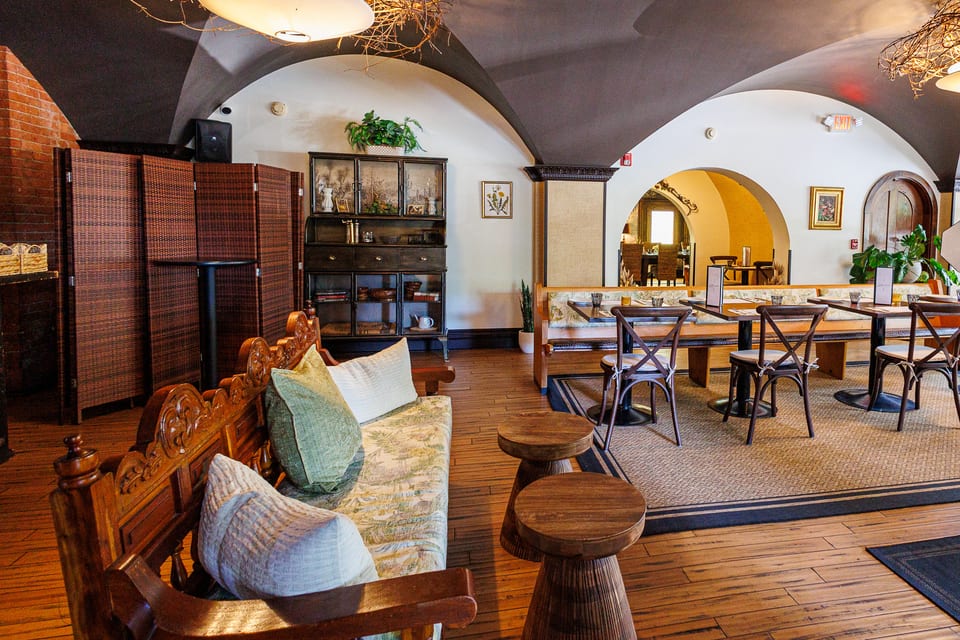 The Alexander lower-level lounge — vaulted ceilings, carved-wood settee with green cushions, built-in hutch, and banquette tables set beneath an archway