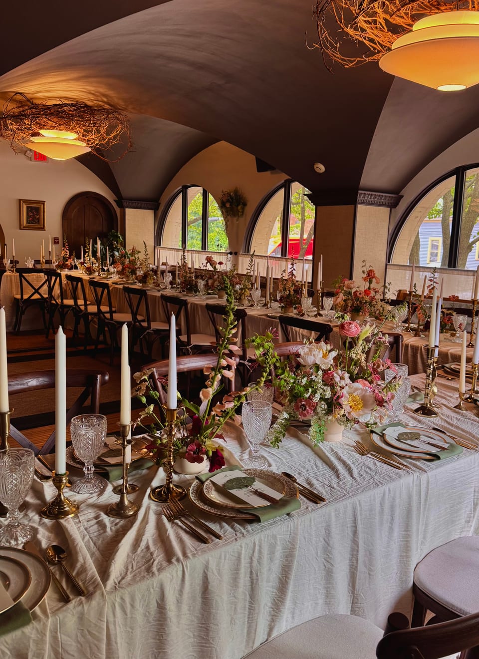Long banquet table with a runner of pink florals, candles, and crystal glassware in the arched-window dining room