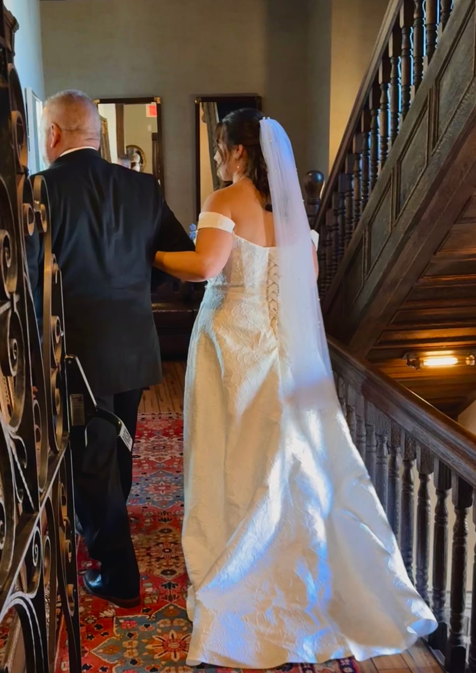 Bride and father walking up the staircase, train flowing behind