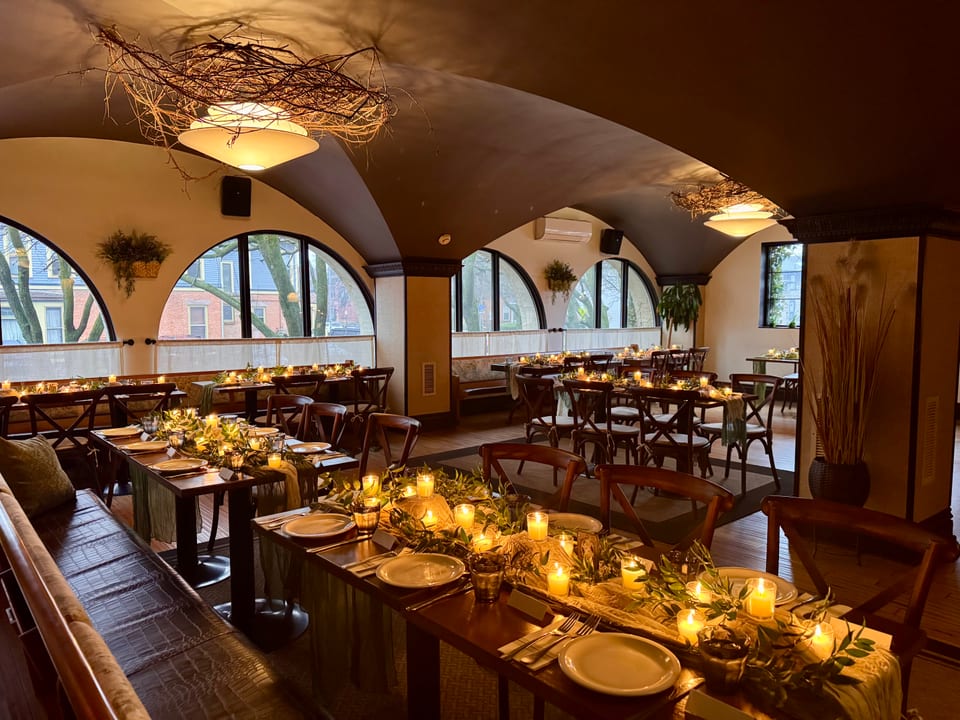 Main dining room set for an evening event — long tables with green runners, candles, and arched windows