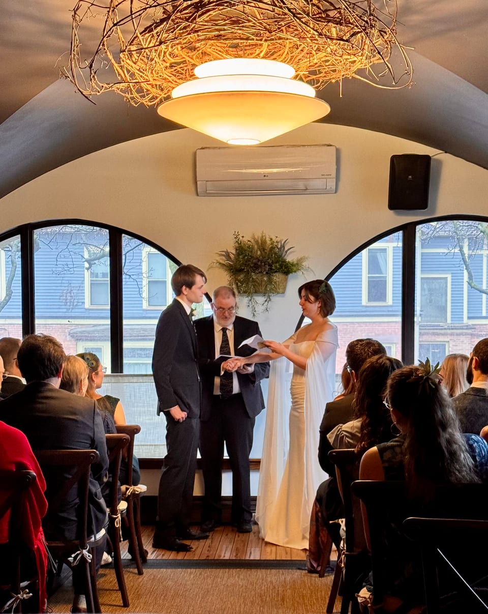 Wedding ceremony in the turret — couple at the altar reading vows, guests seated, arched windows behind